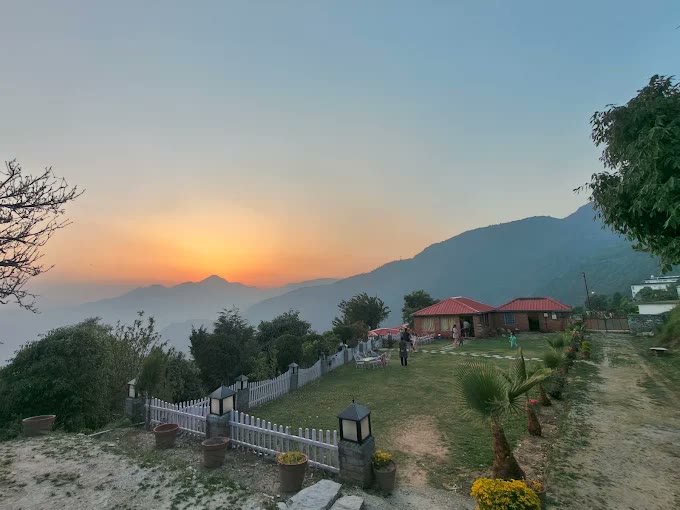 Golden hour sunset over cottages and open lawn at Kanatal Camp